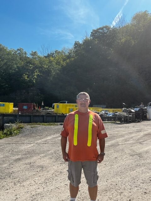 man in orange shirt standing in front of landfill